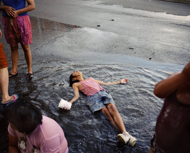 本组图将以雨后的小女孩们为结尾。照片里由于夏季长时间的炎热和少雨，一场大雨后，小女孩欢喜的躺在马路上的积水中，享受片刻的清凉。